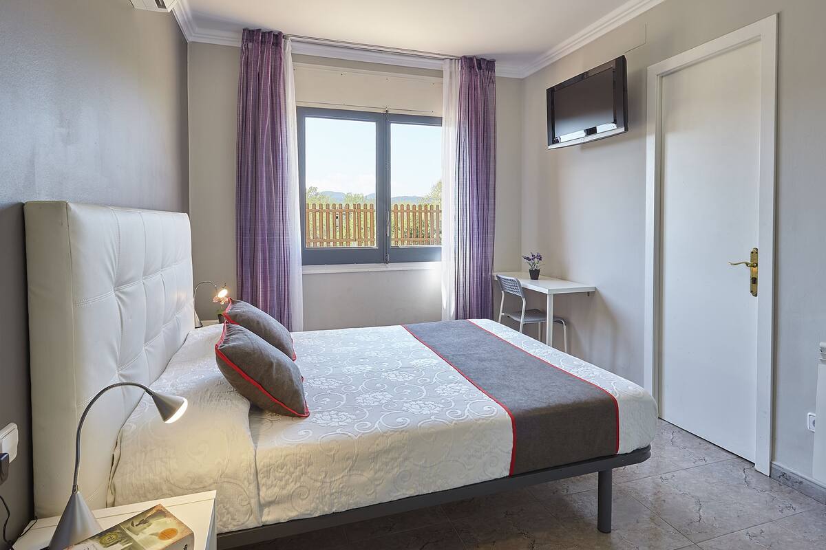 A neatly arranged bedroom with a bed, bedside lamp, and a small desk with a chair.