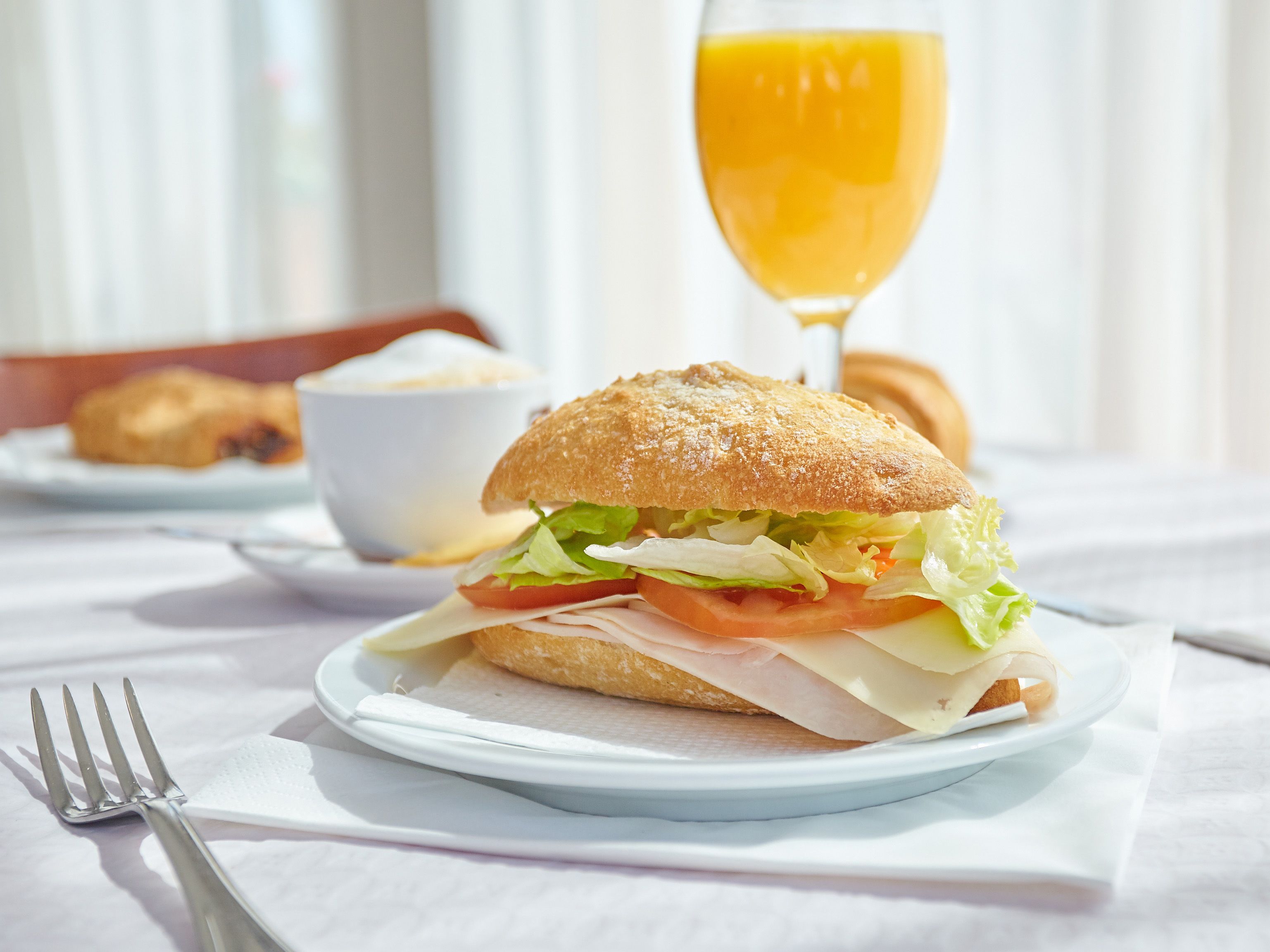 A sandwich on a plate with a glass of orange juice in the background.