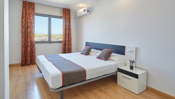 A modern bedroom with a bed, nightstand, and window. - Hostal Mas Ferrer (Cornella del Terri)