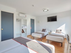 A hotel room with two single beds, a wardrobe, a TV, and a small desk. - Hostal Mas Ferrer (Cornella del Terri)