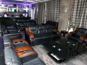 A lobby with leather sofas, a coffee table, and a bar area with a TV screen. - Jonaith Hotels & Suites (Lekki)