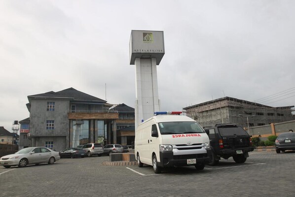 A white ambulance parked in front of a building with a sign reading "HOTEL & SUITES". - Jonaith Hotels & Suites (Lekki)