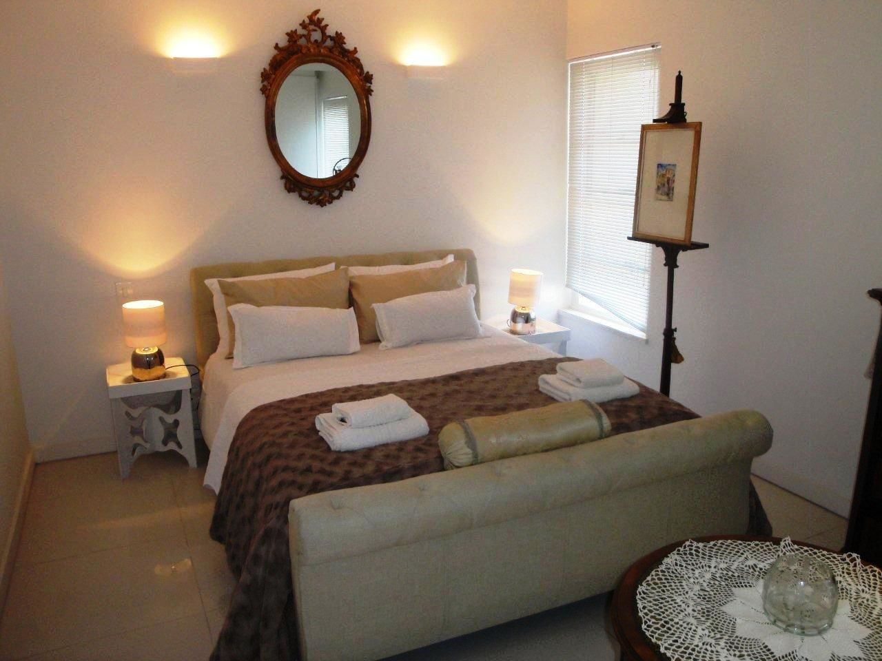 A neatly arranged bedroom with a bed, bedside lamps, a bedside table, a chair, and a bedside table with a decorative item.