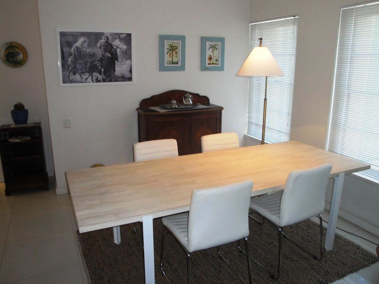 Ein Essbereich mit einem Holztisch, weißen Stühlen, einer kleinen Kommode und zwei an der Wand hängenden Bildern.