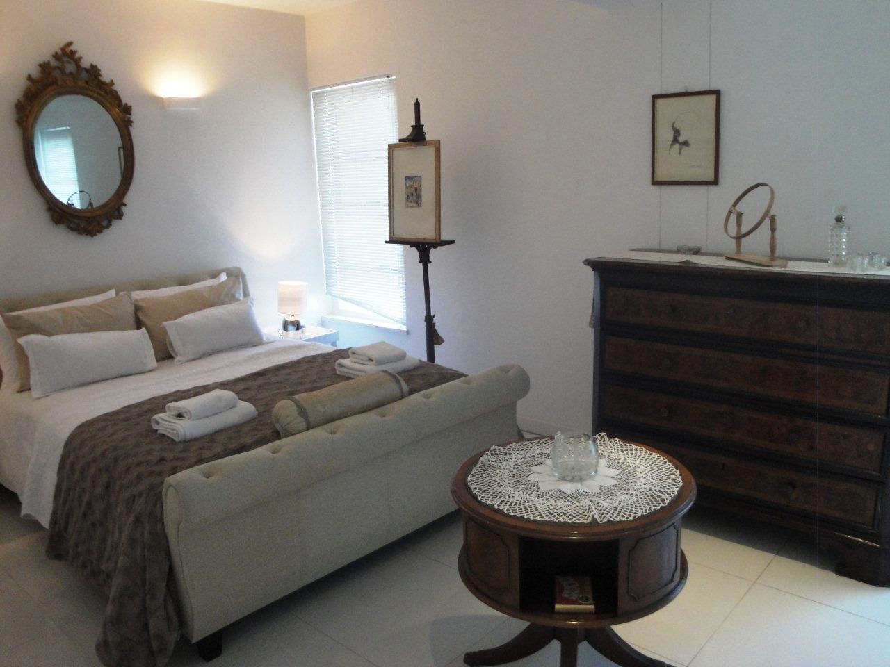 Une chambre à coucher comprenant un lit, une table de chevet, une commode et une petite table ronde surmontée d’un chemin de table.
