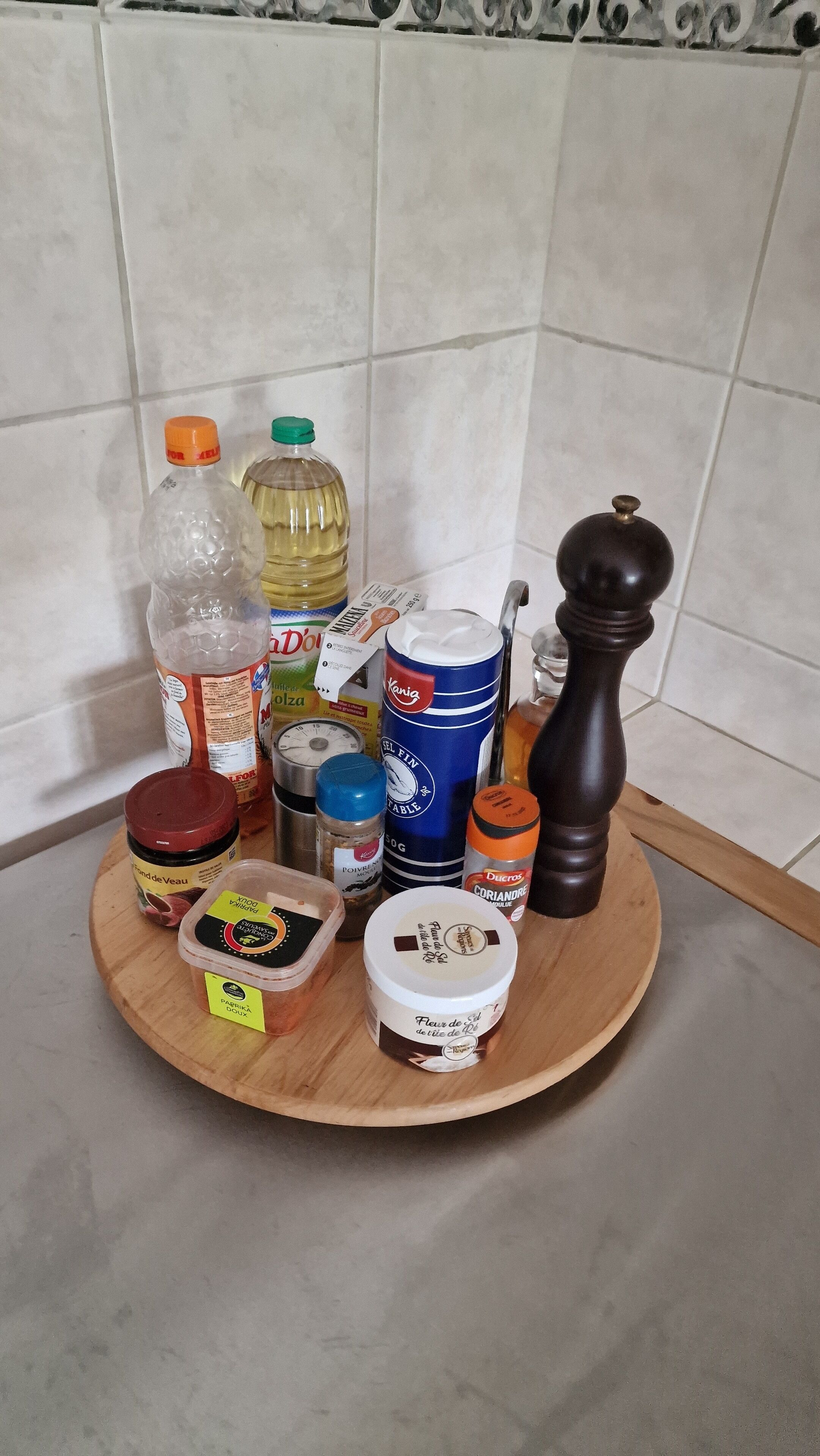 Una tabla de madera con distintos utensilios de cocina, como un salero, un molinillo de pimienta, una botella de aceite, una lata de cerveza y un frasco de mermelada.