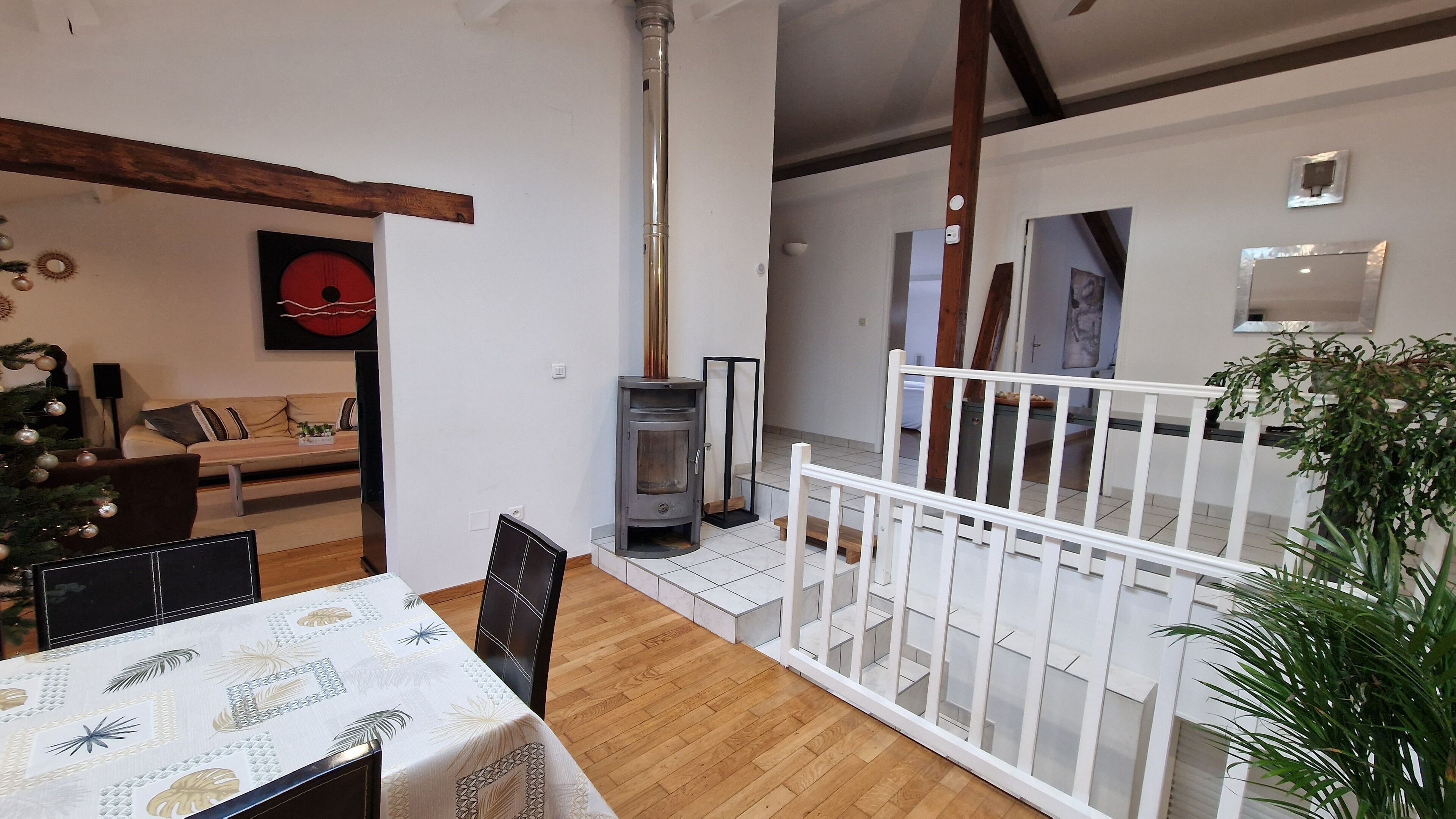 Un salon chaleureux avec une cheminée, un coin repas avec une table dressée pour deux personnes, et un escalier menant à l’étage supérieur.