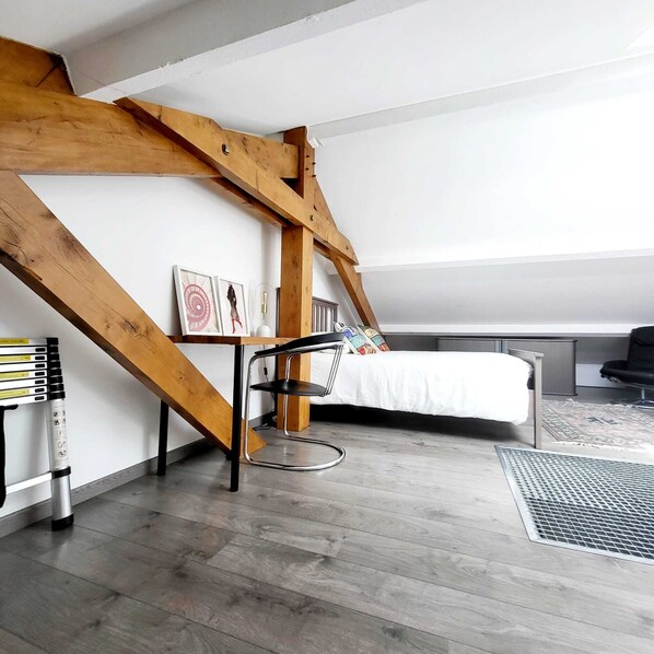 Un dormitorio tipo loft con techo inclinado, una cama, una silla y un escritorio con lámpara.