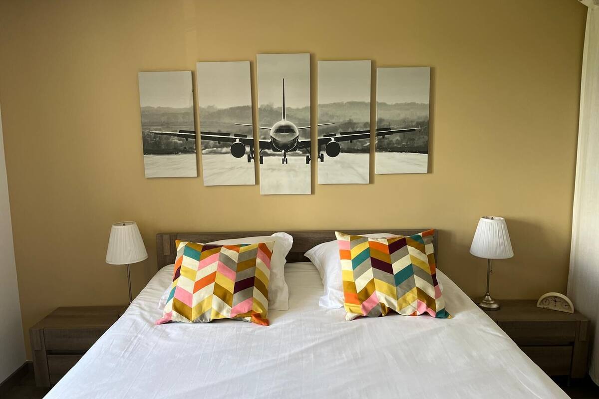 Ein Hotelzimmer mit einem großen Bett, zwei Nachttischen, einem an der Wand hängenden Foto eines Flugzeugs und zwei Lampen.
