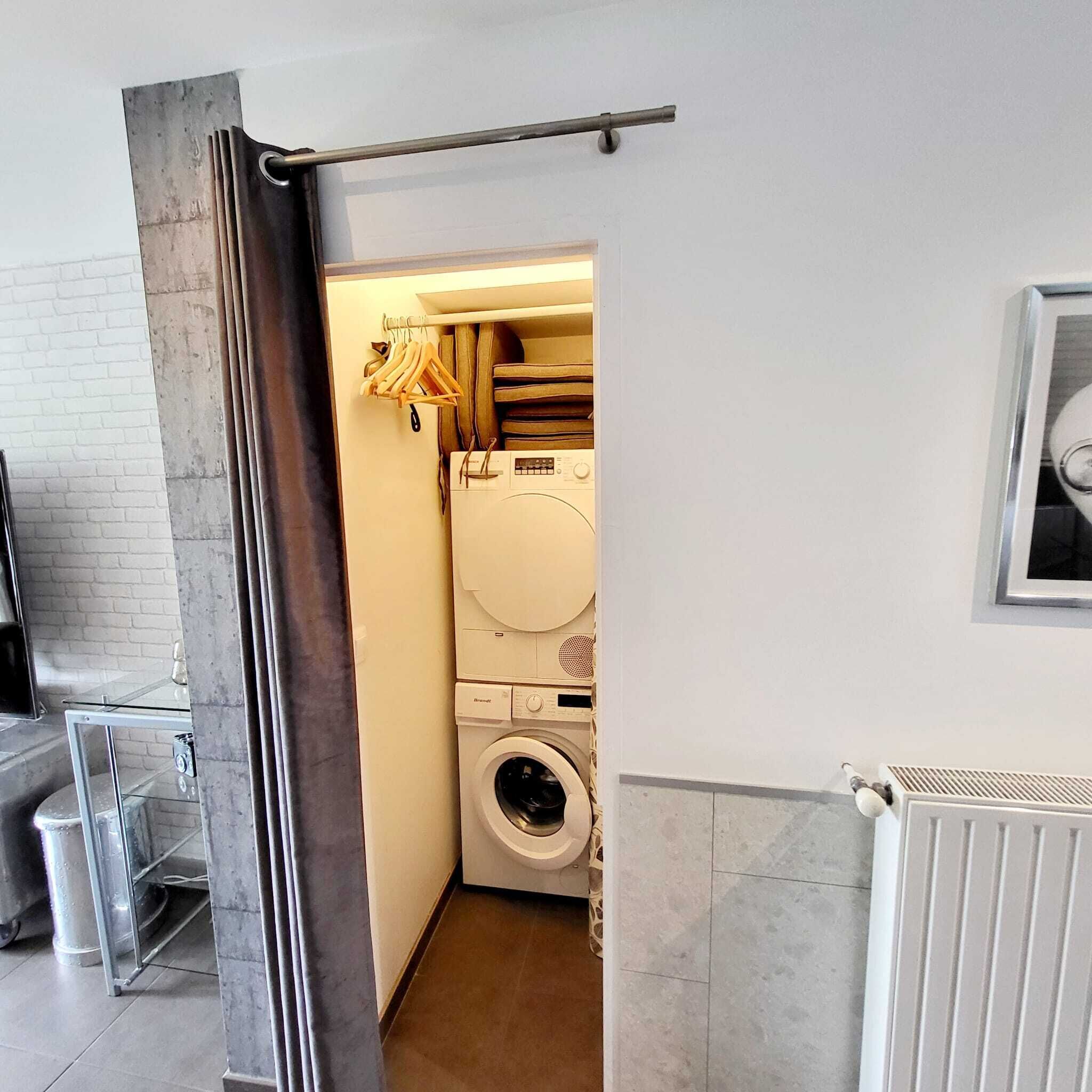 A laundry room with a washing machine and dryer, a drying rack with clothes, and a radiator.