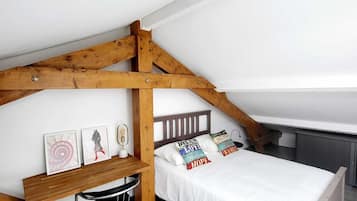 A loft bedroom with a sloped ceiling, wooden beams, a bunk bed, a small desk, and a chair.