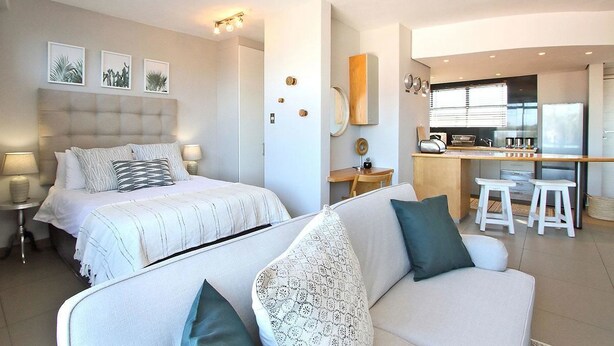 A modern hotel room with a bed, a sofa, a desk, and a kitchenette. - Morakani (Cape Town)