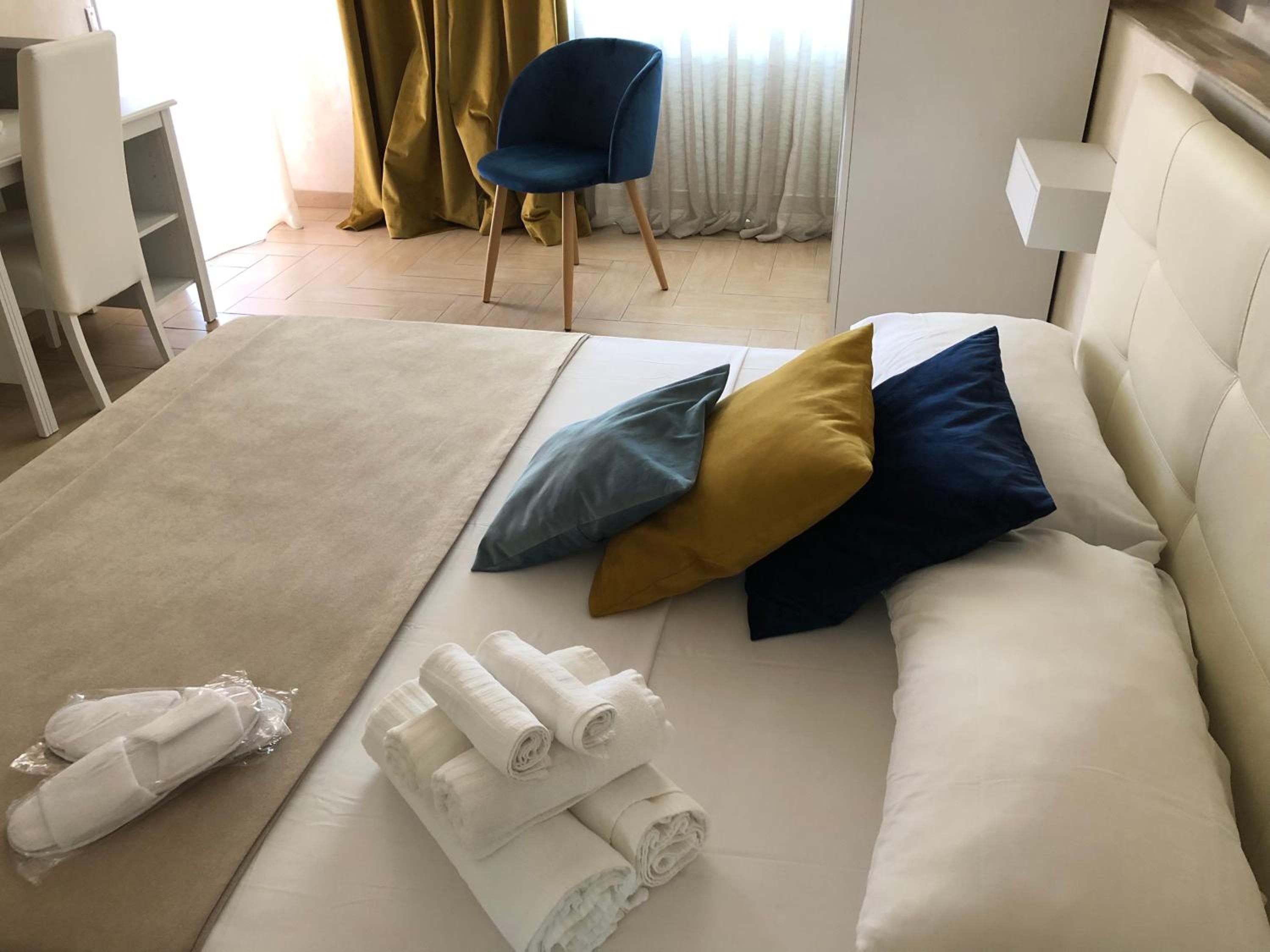 Una cama bien hecha con almohadas y toallas enrolladas, una silla y una mesita de noche en una habitación de hotel.