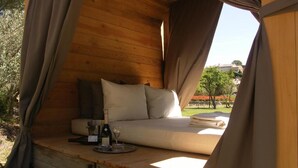 Een gezellige houten tent met een bed, kussens, een fles wijn en een glas op een houten tafel.