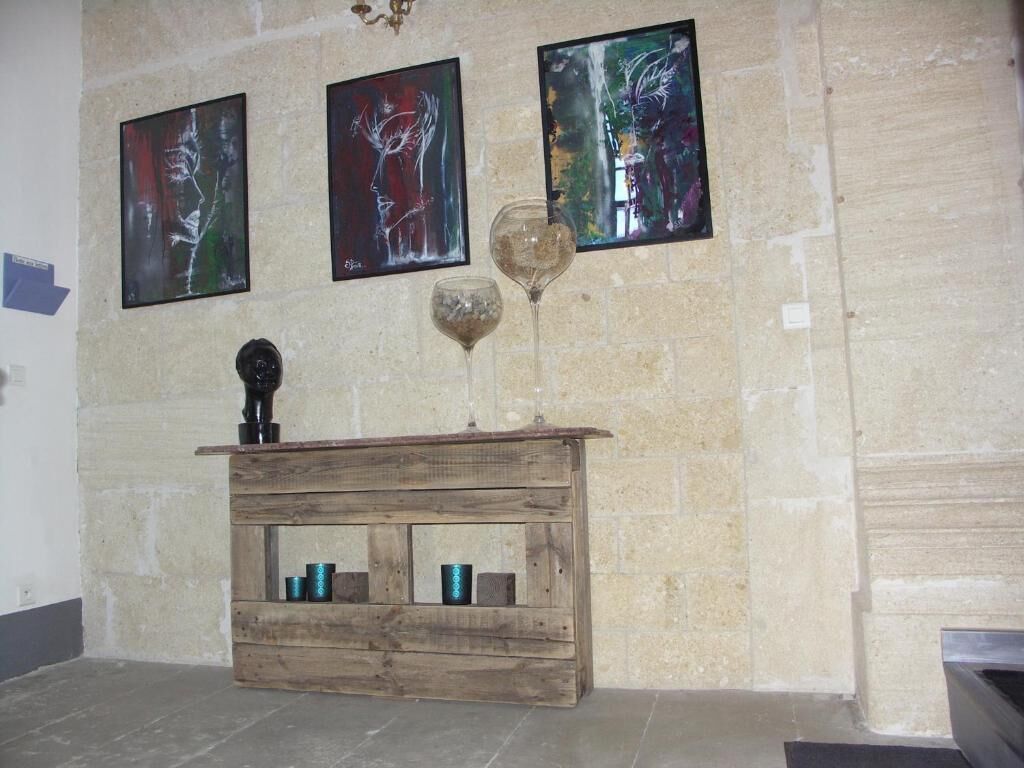 A rustic wooden bench with a glass and a sculpture against a stone wall.