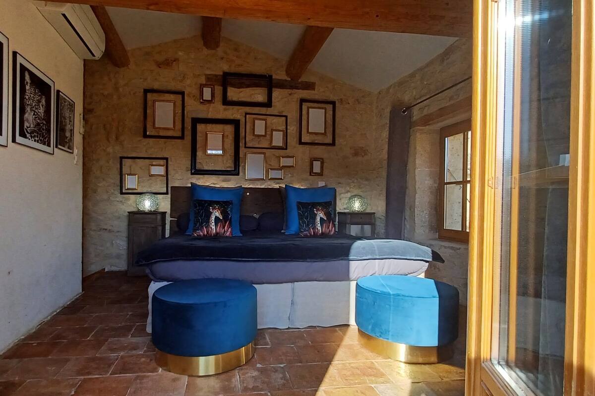 Een slaapkamer met een stenen muur, een bed met blauw-witte beddengoed, en ingelijste foto's aan de wand.