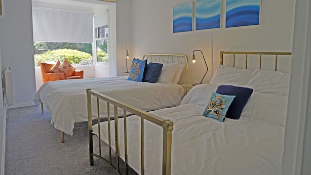 A bedroom with two beds, a window with a view of greenery, and a ceiling light fixture. - Birch at Somerhill (Hove)