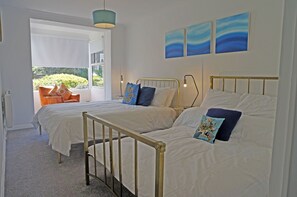 A bedroom with two beds, a window with a view of greenery, and a ceiling light fixture.