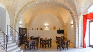 Un coin repas doté d’un plafond en forme d’arc en pierre, de tables et de chaises en bois, d’un buffet et d’un téléviseur à écran plat fixé au mur.