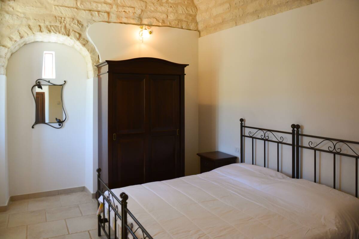 A bedroom with a bed, a wardrobe, a nightstand, and a mirror.