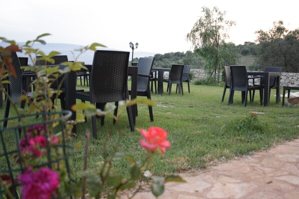 Espace extérieur aménagé avec des tables et des chaises, un mur en pierre et une zone herbeuse agrémentée de fleurs.