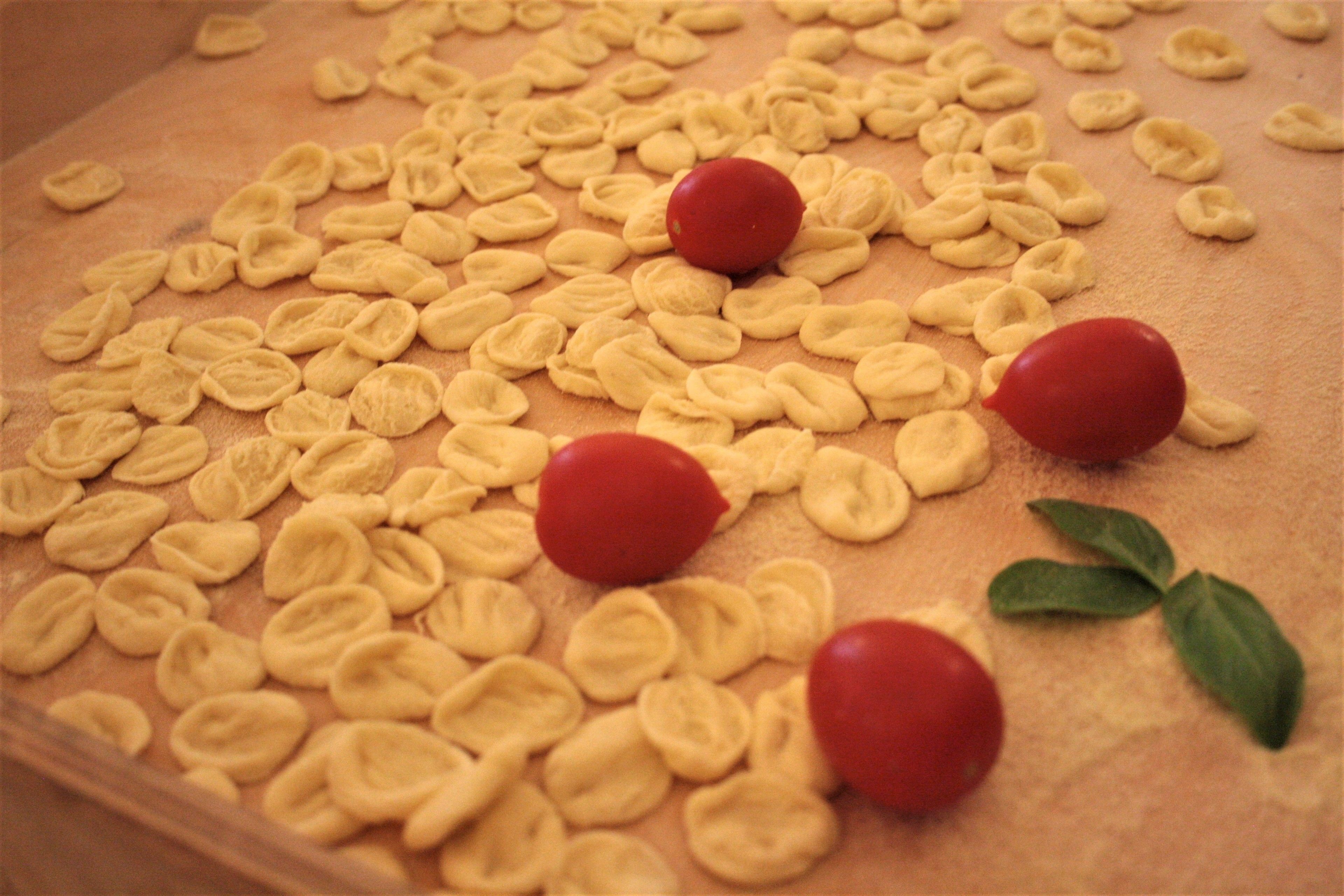 Superficie de madera con formas de pasta y algunos objetos rojos.
