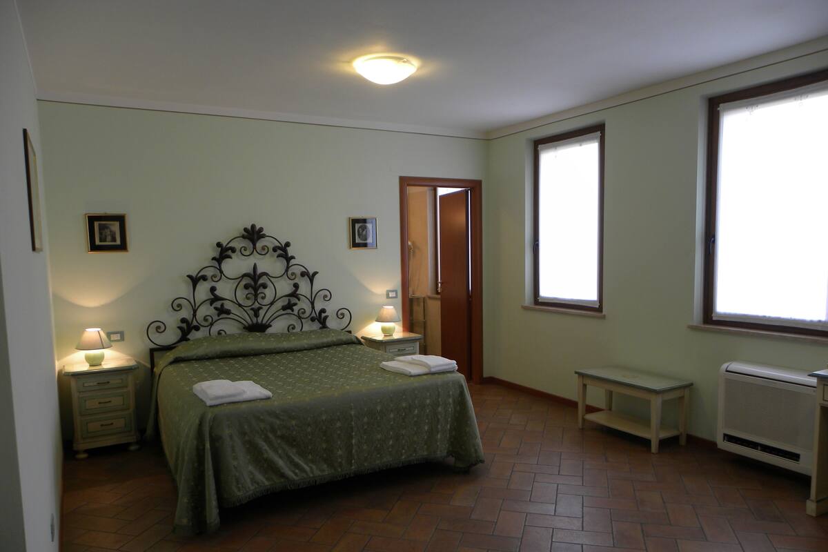Un dormitorio con cama, lámparas de noche, un radiador y una ventana.