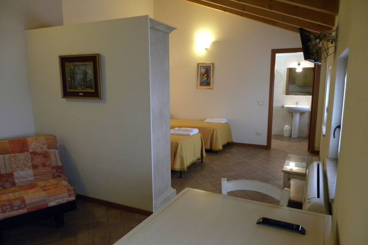 Habitación de hotel con cama, una pequeña mesa, un sofá y un baño visible a través de una puerta abierta.