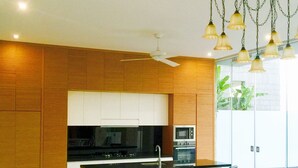 A modern kitchen with a central island, two bar stools, a ceiling fan, and pendant lights.