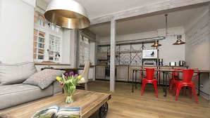 A spacious living area with a sofa, a coffee table with magazines, a vase of flowers, and a kitchen in the background. - Patio Apartamenty (Gdansk)