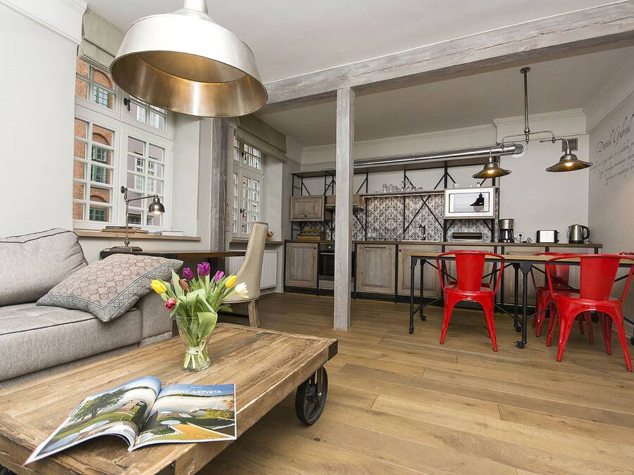 Amplia sala de estar con un sofá, una mesa de centro con revistas, un jarrón de flores y una cocina al fondo.