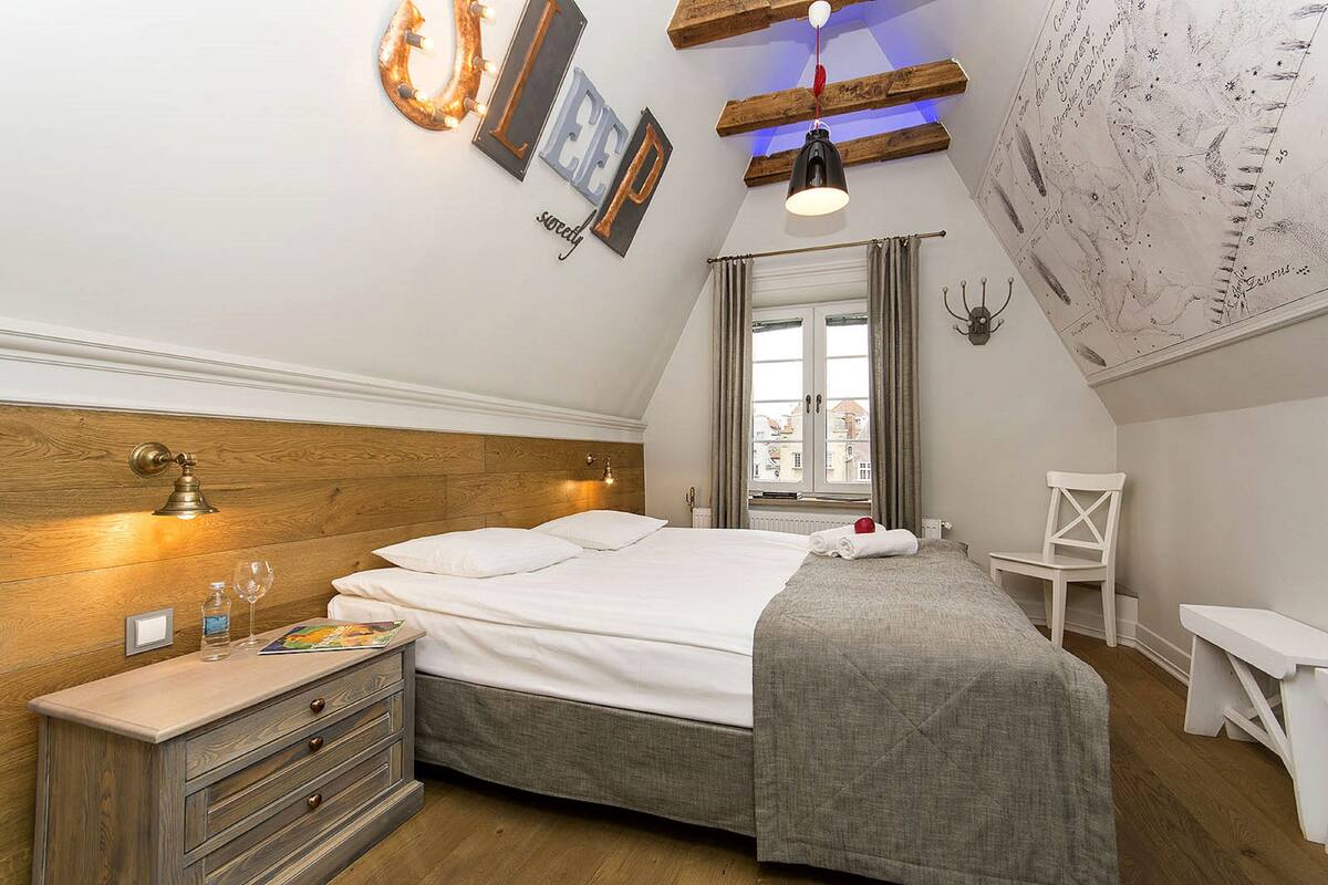 Un dormitorio con cabecera de madera, cama con ropa de cama blanca, mesita de noche con una botella y un vaso, y un mapa en la pared.