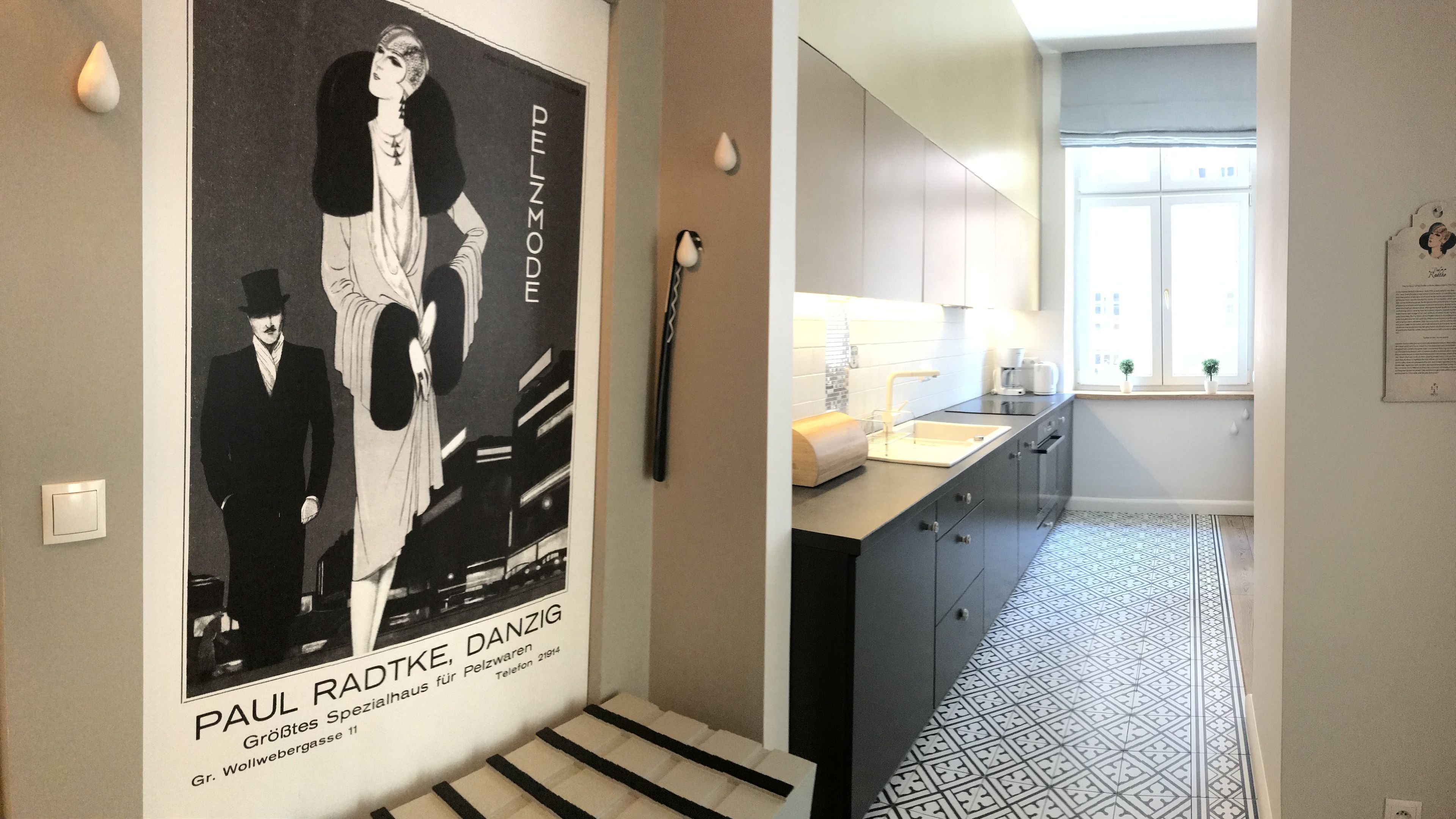 Uma cozinha moderna com chão de azulejos preto e branco, bancada branca e janela com vista para edifícios.