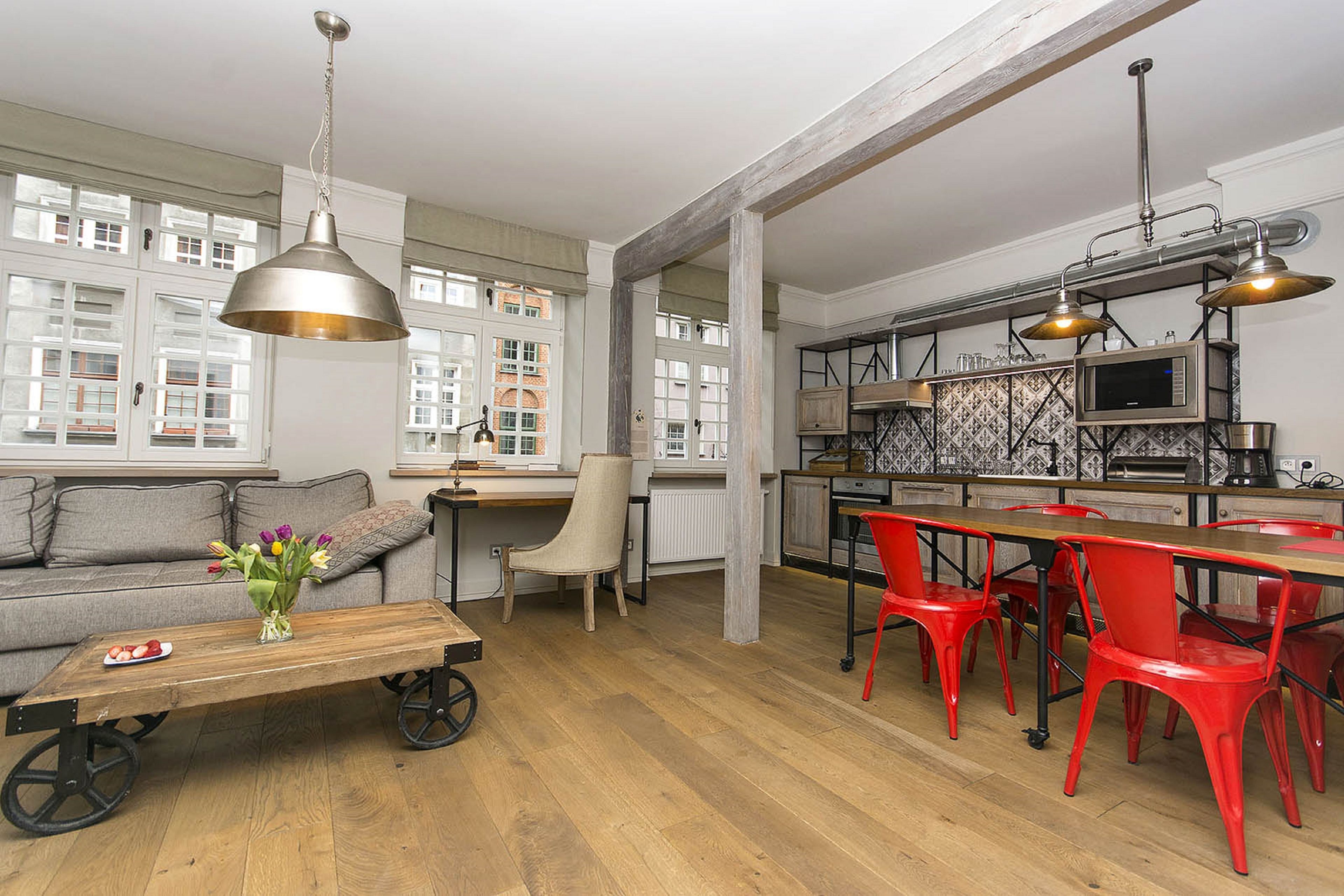 A modern kitchen with a dining area, featuring a wooden table, red chairs, and a large window with a view of buildings.