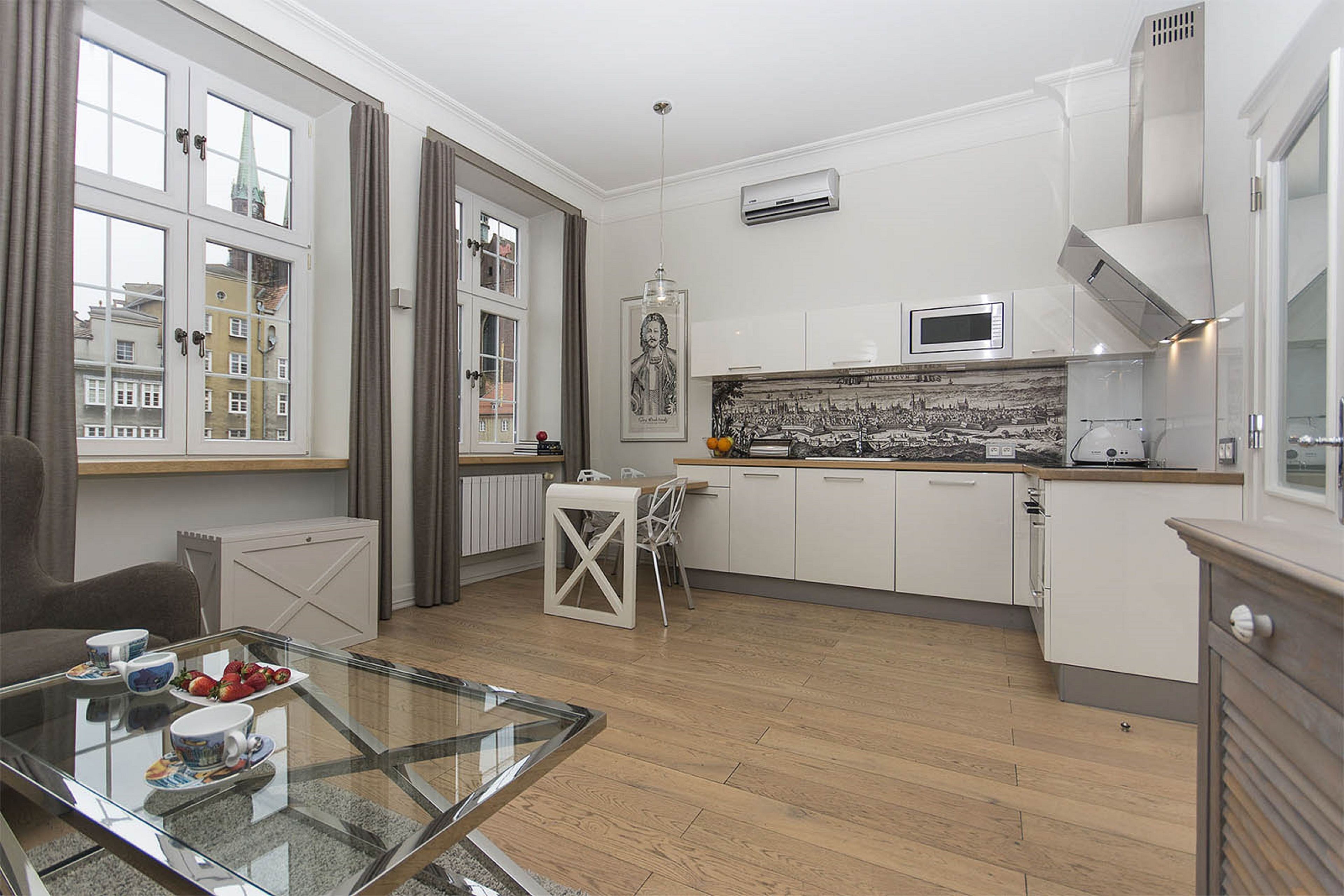 Una cocina moderna con armarios blancos, microondas y un comedor con mesa y sillas de vidrio.