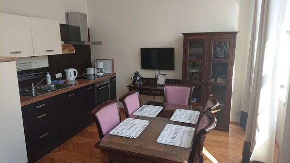 Una cocina compacta con electrodomésticos modernos, una mesa de comedor con manteles individuales y un televisor en la pared.