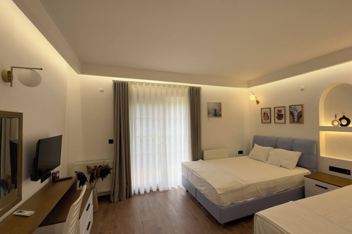 Habitación de hotel con dos camas, televisión, escritorio y ventana con cortinas.