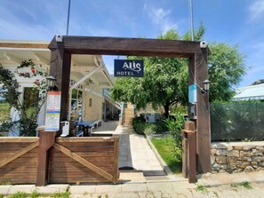 A wooden archway with a sign reading "ALS HOTEL" leading to a covered outdoor seating area with tables and chairs.