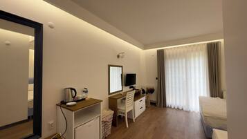 Habitación de hotel con escritorio de madera, televisor, cama y un ventanal grande con cortinas.