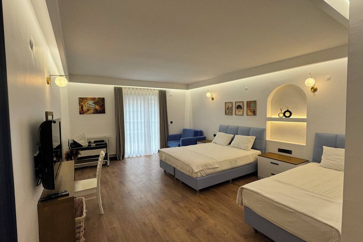 Habitación de hotel con dos camas, un escritorio con silla, televisor y ventana con cortinas.