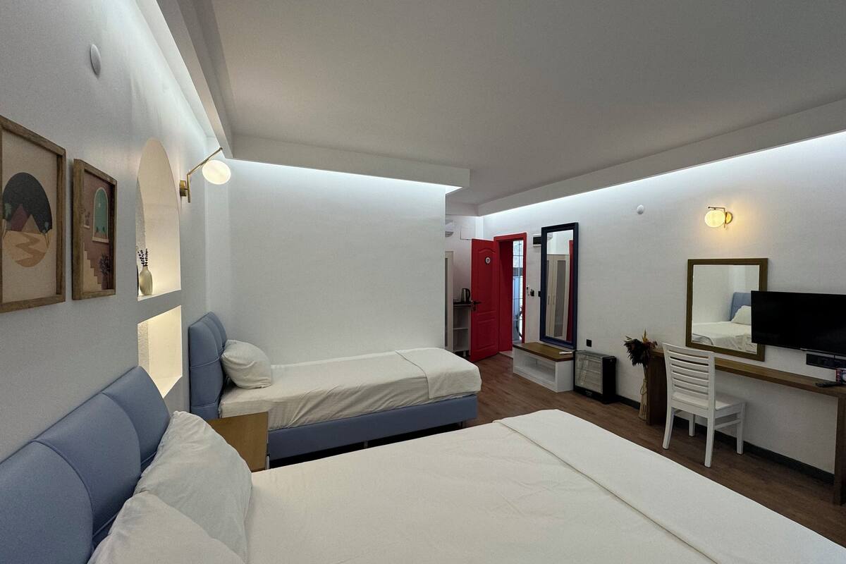 Habitación de hotel con dos camas, un escritorio con televisor, un espejo y un armario.
