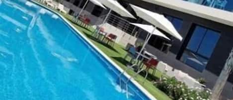 Um hotel moderno com piscina, várias varandas e áreas de estar ao ar livre.