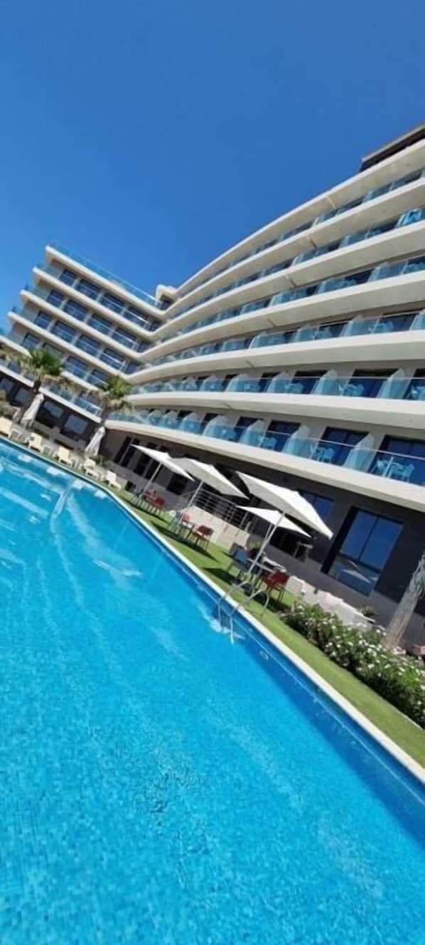 A modern hotel with a pool, multiple balconies, and outdoor seating areas.