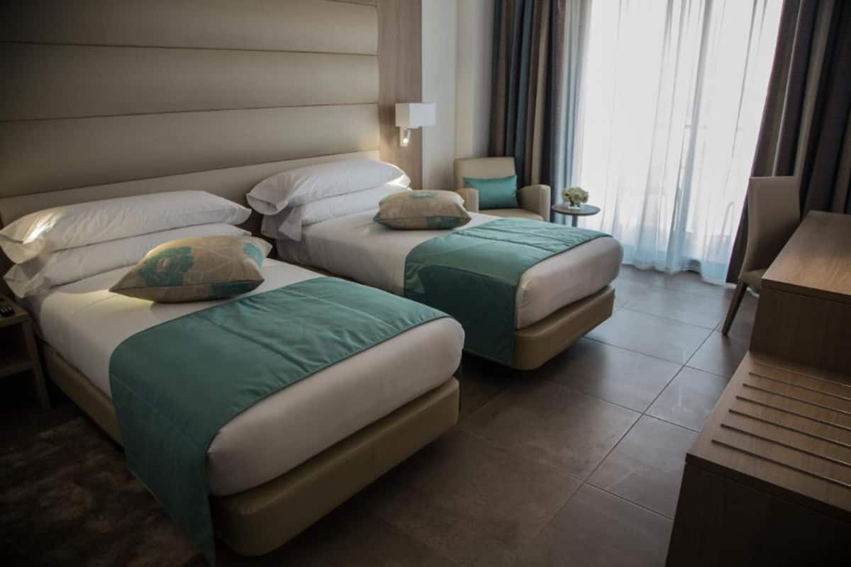 Een hotelkamer met twee bedden, een stoel, een klein tafeltje en een bureau.