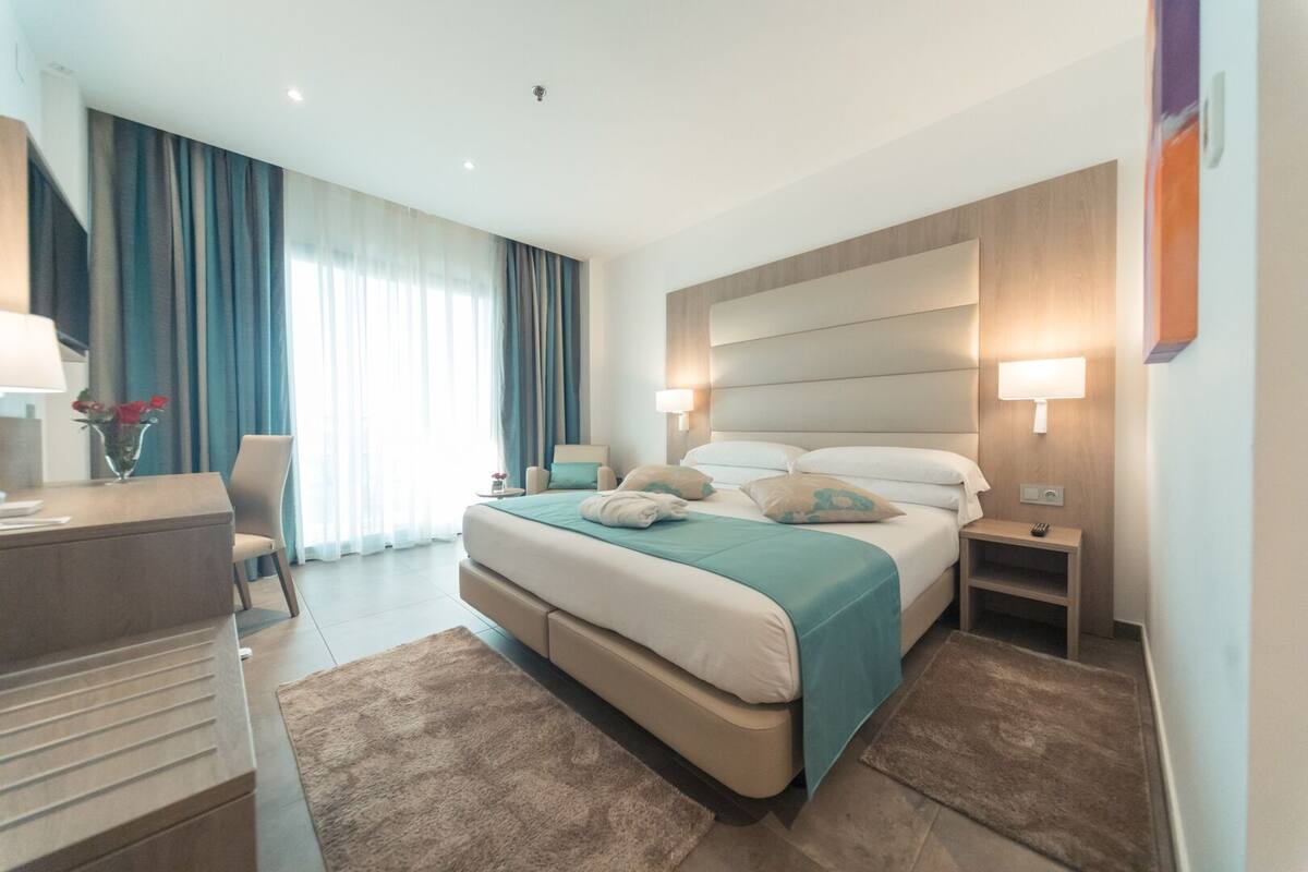 Een moderne hotelkamer met een groot bed, nachtkastjes, een bureau en een stoel.