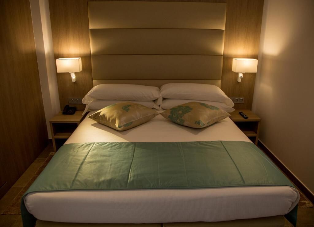 Una habitación de hotel con una cama grande, dos lámparas de noche y un cabecero de madera.