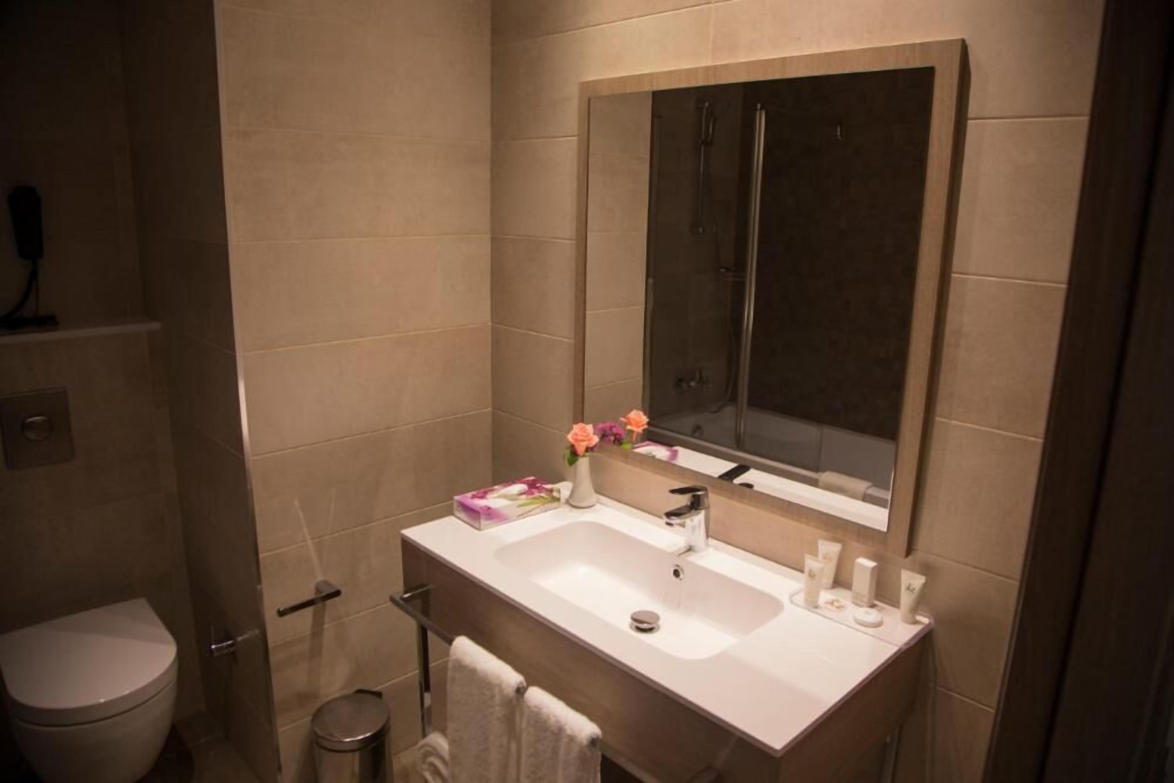 Un baño con un lavamanos blanco, un espejo encima y una ducha visible al fondo.