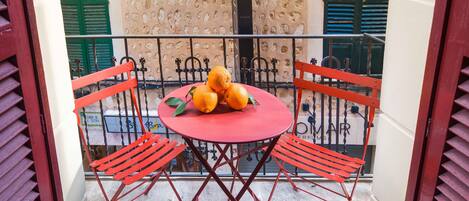 A small outdoor balcony with a round table and four red chairs. There are three oranges on the table.
