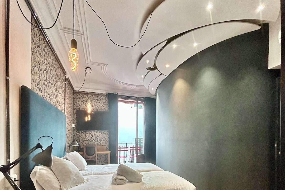 A modern bedroom with a bed, bedside table, lamp, and a view of the outside.