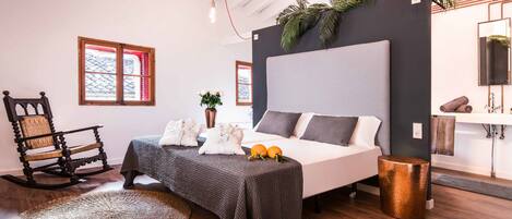 A bedroom with a bed, a rocking chair, a potted plant, and a bathroom with a sink and towel rack.